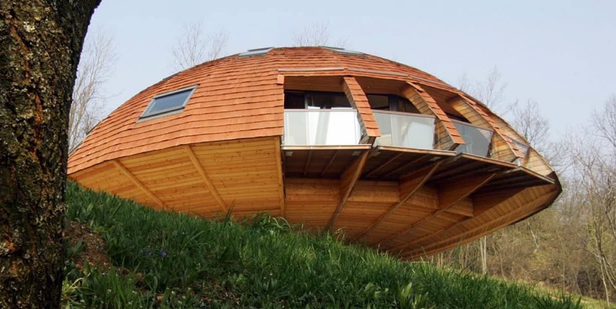 Maison Domespace : coque en bois courbé couverte de bardeaux, posée sur un talus herbeux
